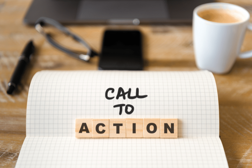 Taccuino aperto su una scrivania con la scritta “Call to Action” composta da lettere in legno, con smartphone, occhiali e una tazza di caffè sullo sfondo.