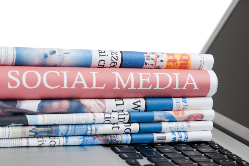Pile di riviste cartacee con la scritta “Social Media” appoggiate su un laptop