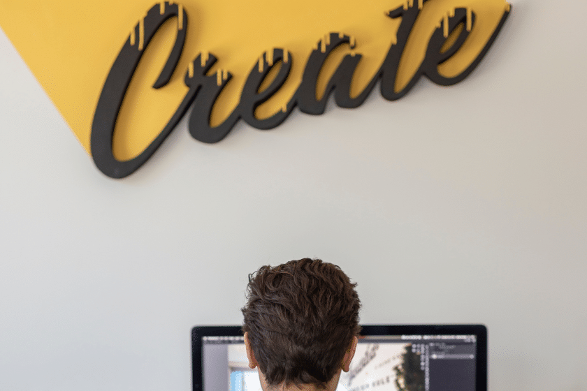 designer al lavoro al computer in studio creativo con insegna create alle spalle