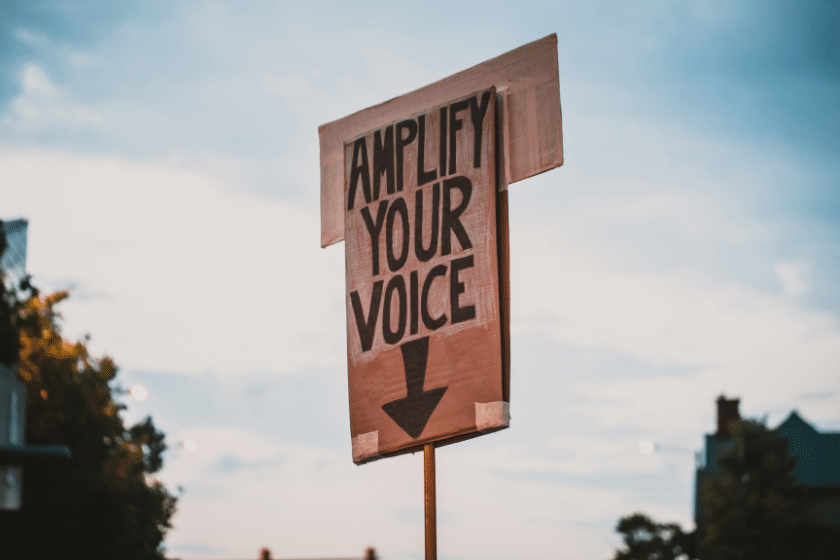 Cartello con scritta amplify your voice tenuto in alto all’aperto