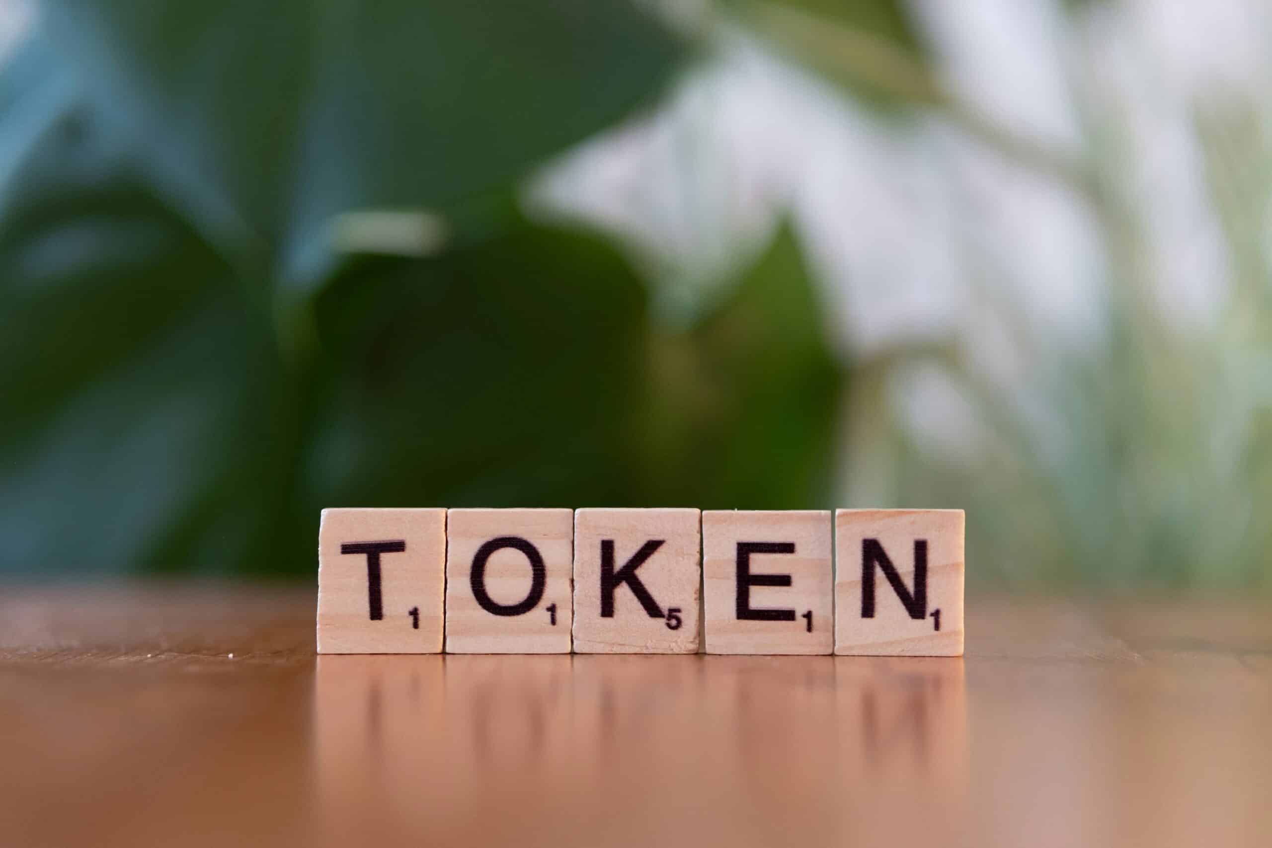 La parola token composta con tessere di legno tipo Scrabble su un tavolo, con fogliame verde sfocato sullo sfondo